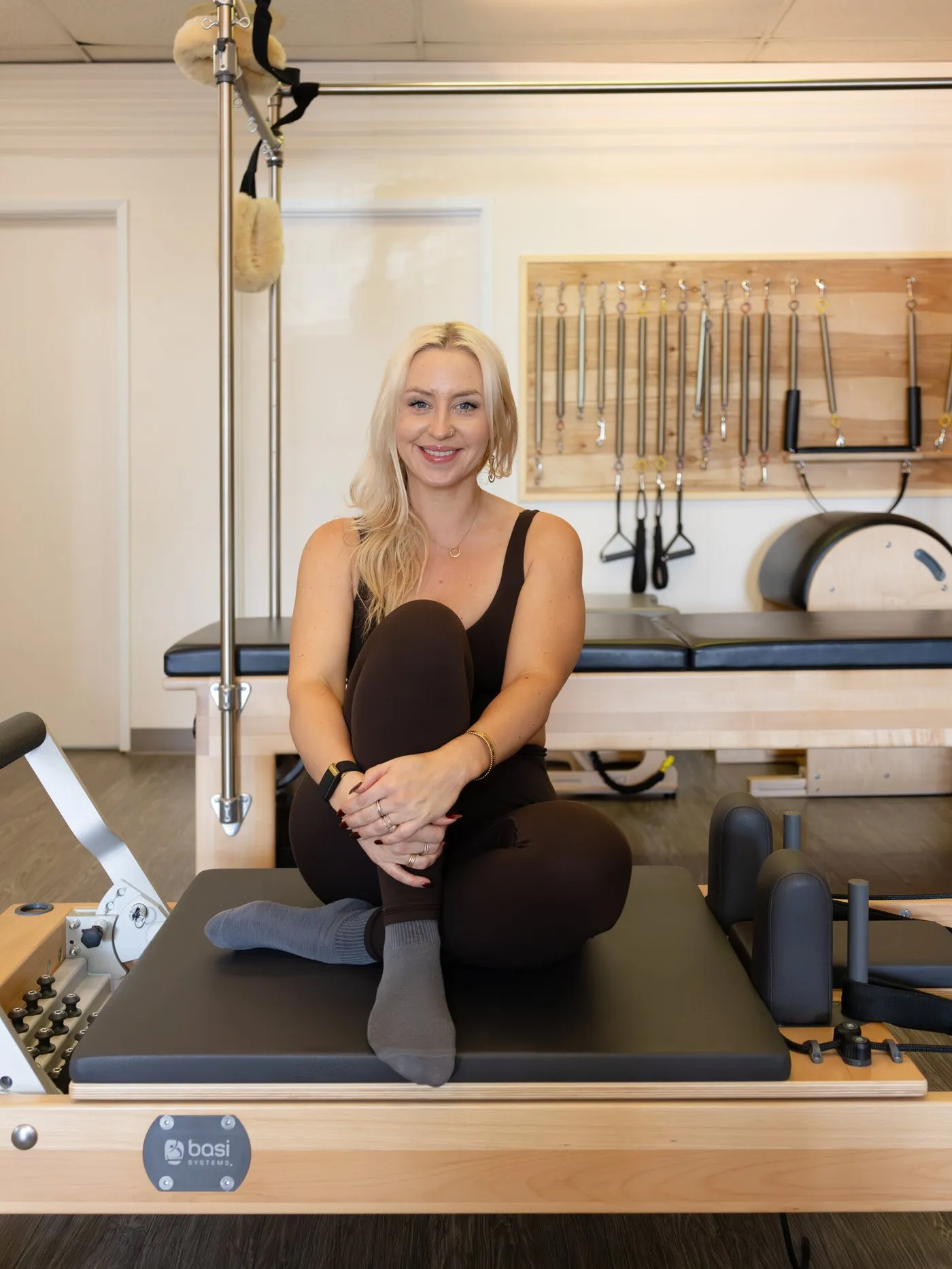 Lauren seated on a reformer in the studio, hands resting on one knee.