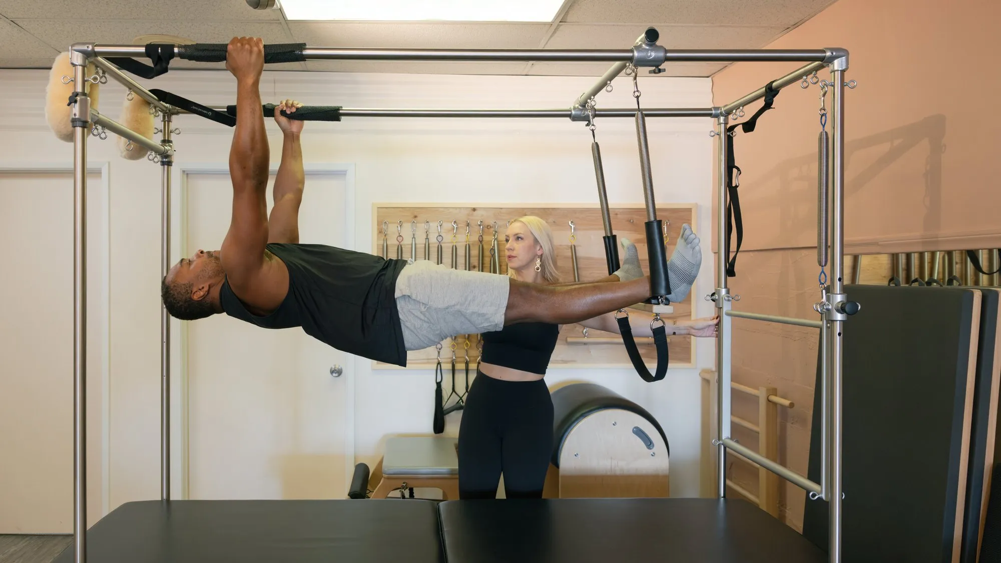 A client hanging horizontally from the Cadillac push-through bar while Lauren spots him from beside the frame.
