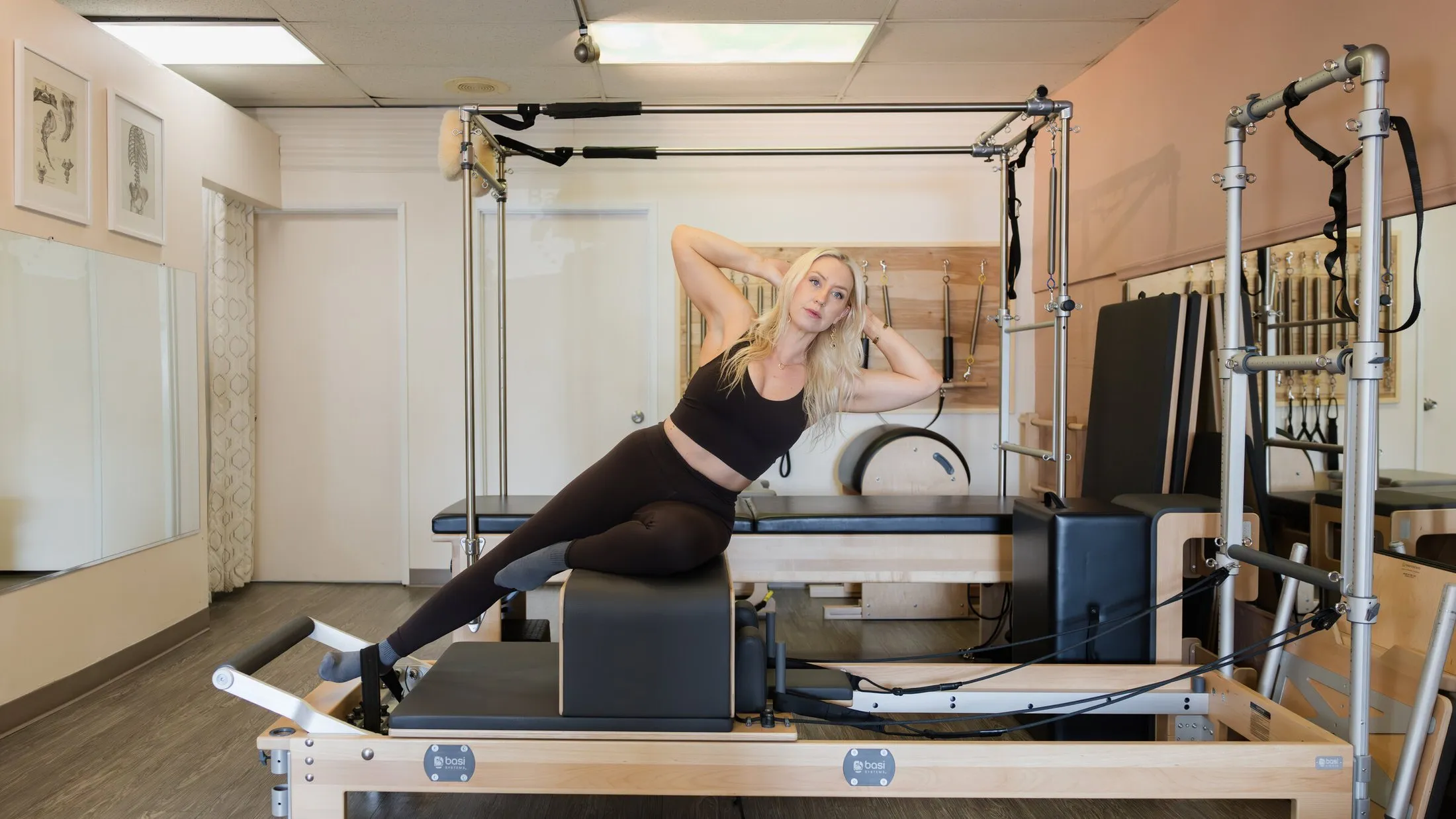The Pilates studio interior, with reformers along a mirrored wall and framed anatomy prints.